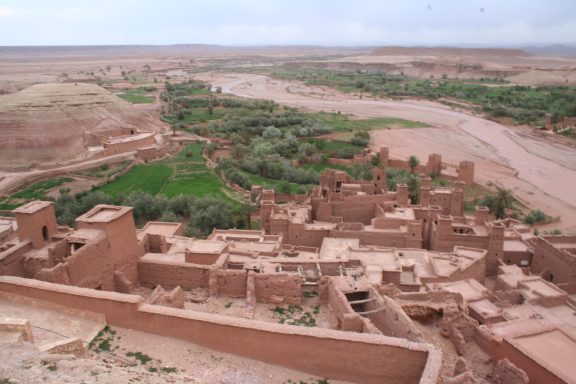Aerial view of ancient mud-brick structures amidst lush green fields and a winding river.
