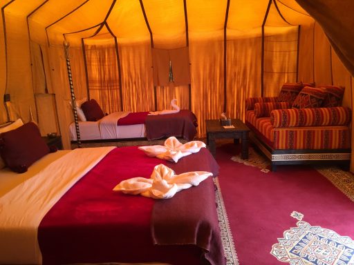 Luxurious tent interior with two beds, a seating area, and warm golden drapes.
