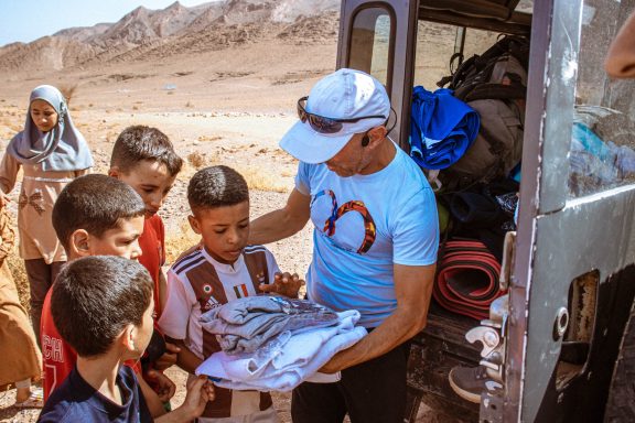 A man hands out clothing to children in a desert setting.