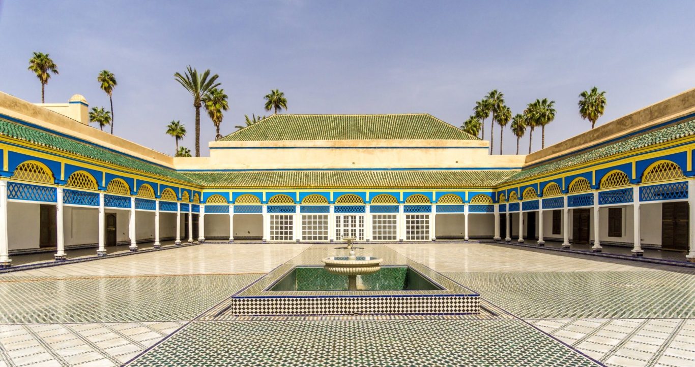 Courtyard with a central fountain, surrounded by palm trees and vibrant mosaic tiles.
