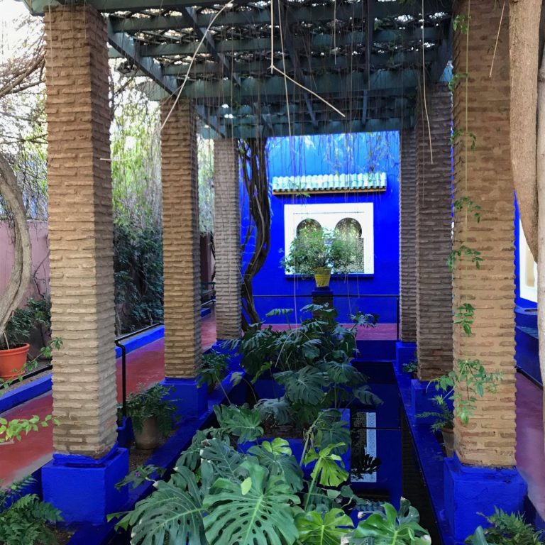 Vibrant blue garden with pillars, plants, and a serene water feature.