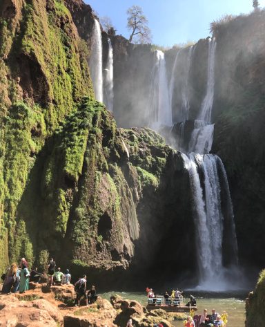 Majestic waterfalls cascading down lush, green cliffs with visitors nearby.